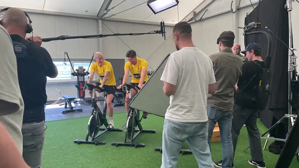 BvB Fußballer traineren vor Kameras auf Fitnessbikes für eine Werbung für EA Sports FC Mobile.