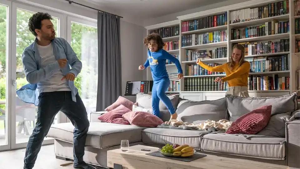 Familie hat Spaß beim Tanzen auf dem Wohnzimmer-Sofa während einer Werbefilmproduktion in Köln.